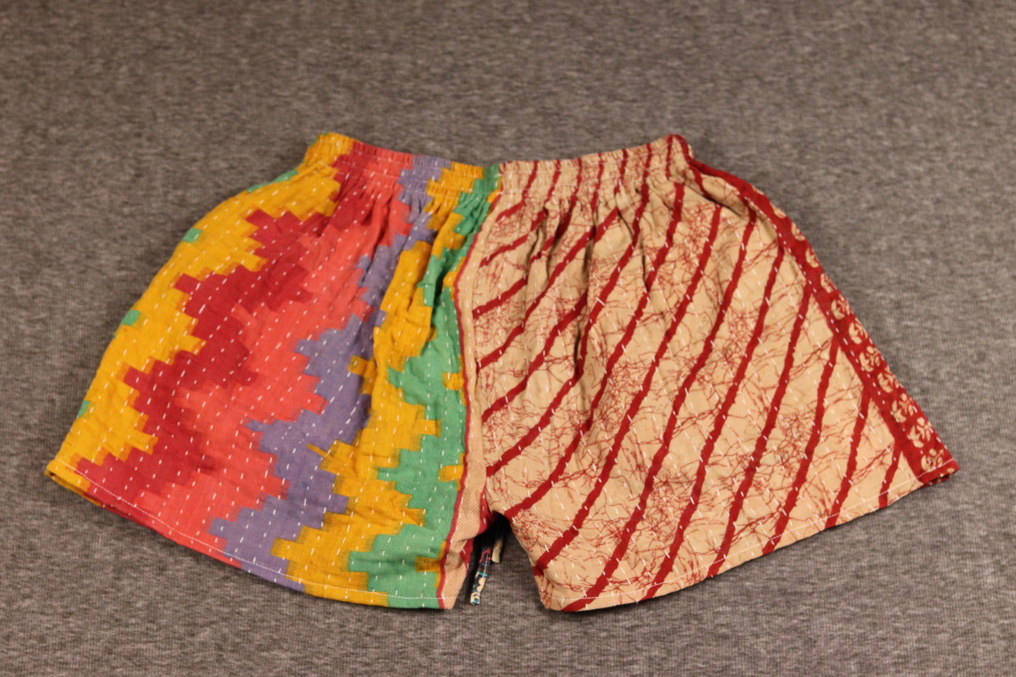 Unisex Kantha shorts with red, orange, green, and cream cotton panels featuring stripes and medallion prints, detailed with Kantha stitching and a drawstring waist.