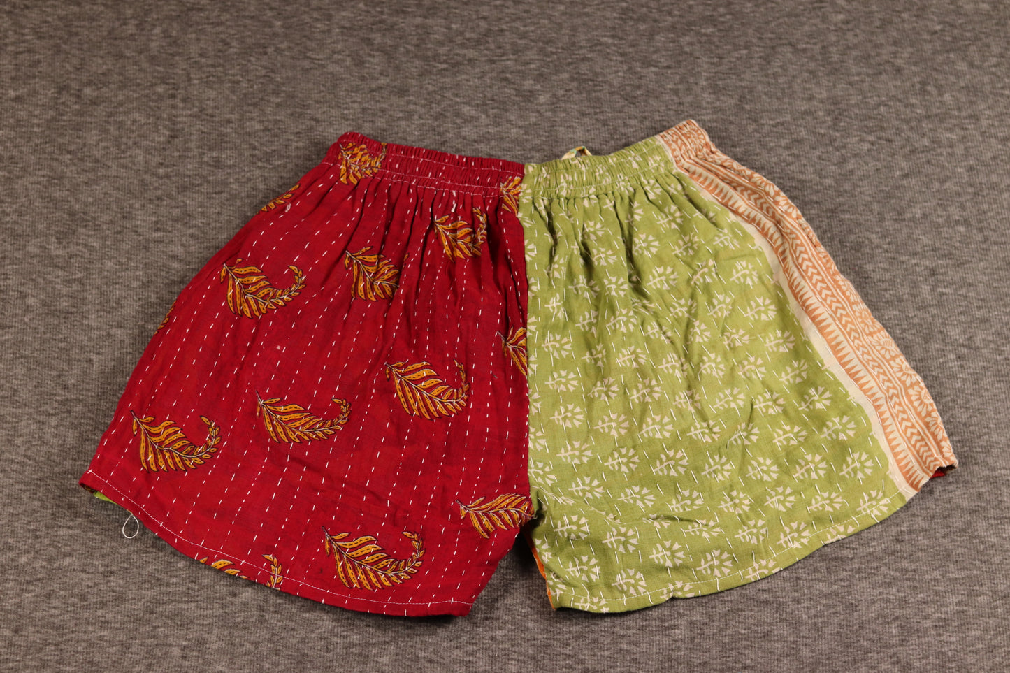 Unisex Kantha shorts with red, green, and cream cotton panels featuring floral and medallion prints, detailed with Kantha stitching and a drawstring waist.