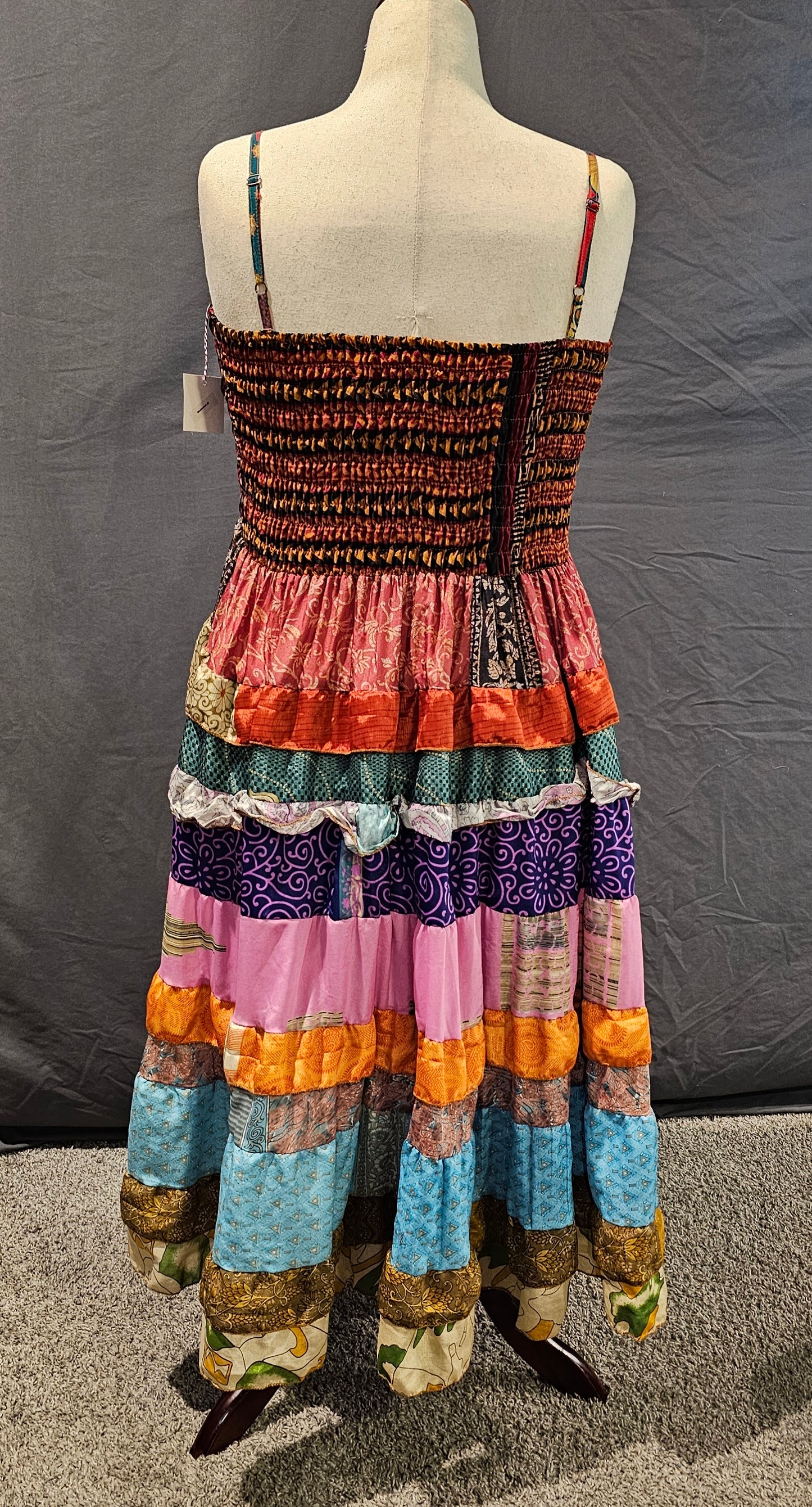 Meadowlark boho patchwork tiered dress in rust, teal, pink, and gold tones with geometric bodice and flowy skirt.