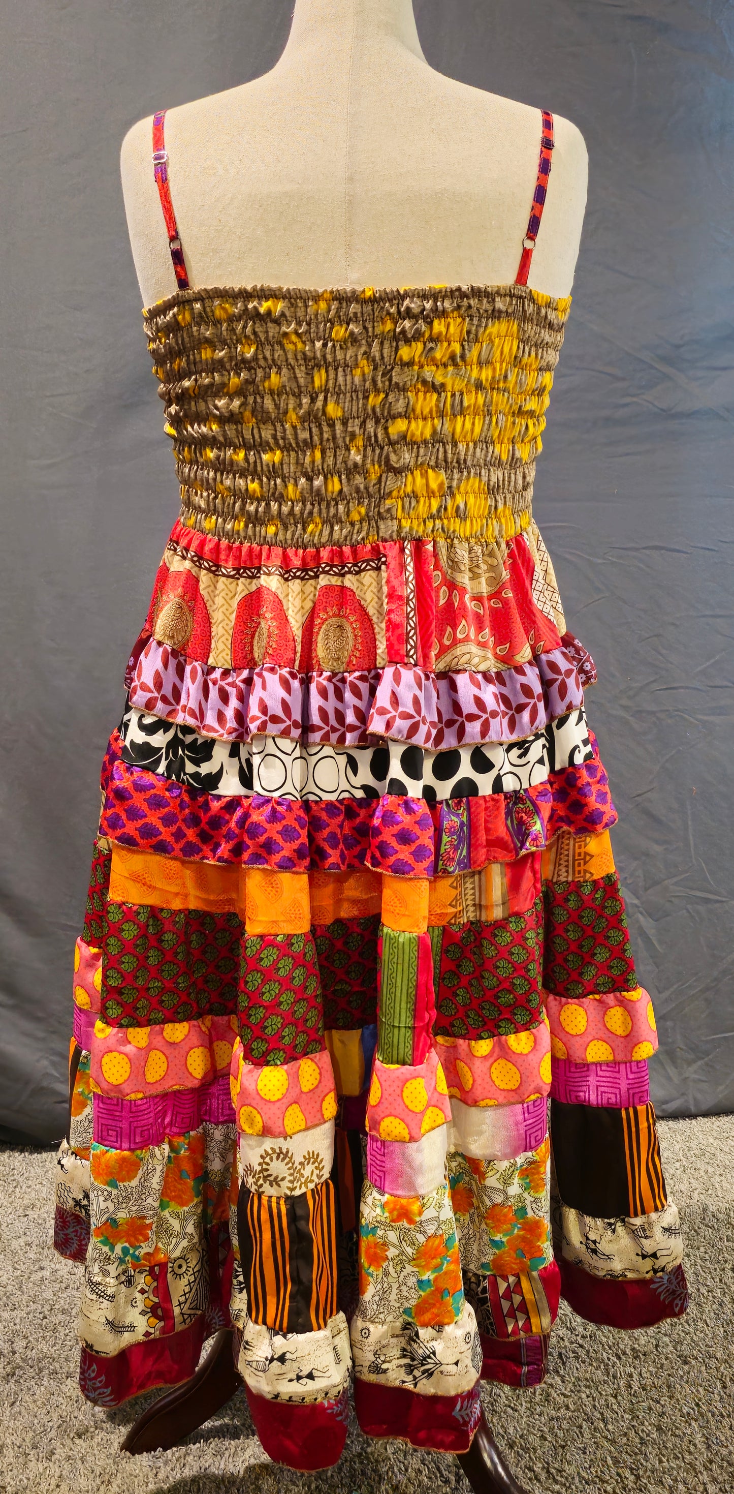 Bohemian patchwork dress with a neutral tan bodice and vibrant red, orange, and yellow tiered skirt, made from recycled sari fabrics.