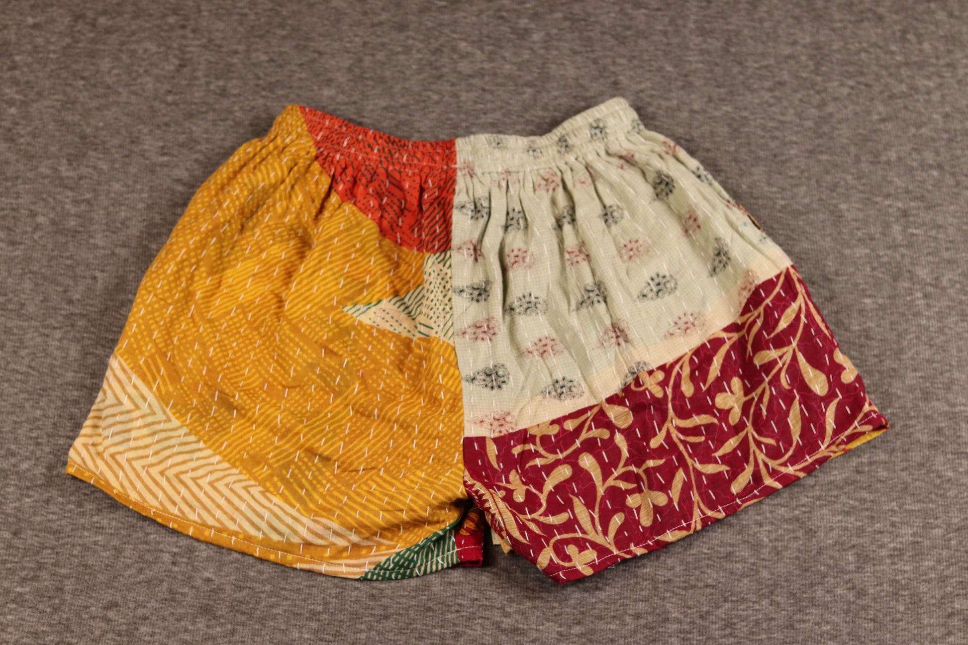 Unisex Kantha shorts with golden yellow and crimson cotton panels featuring chevron and leaf prints, detailed with Kantha stitching and a drawstring waist.