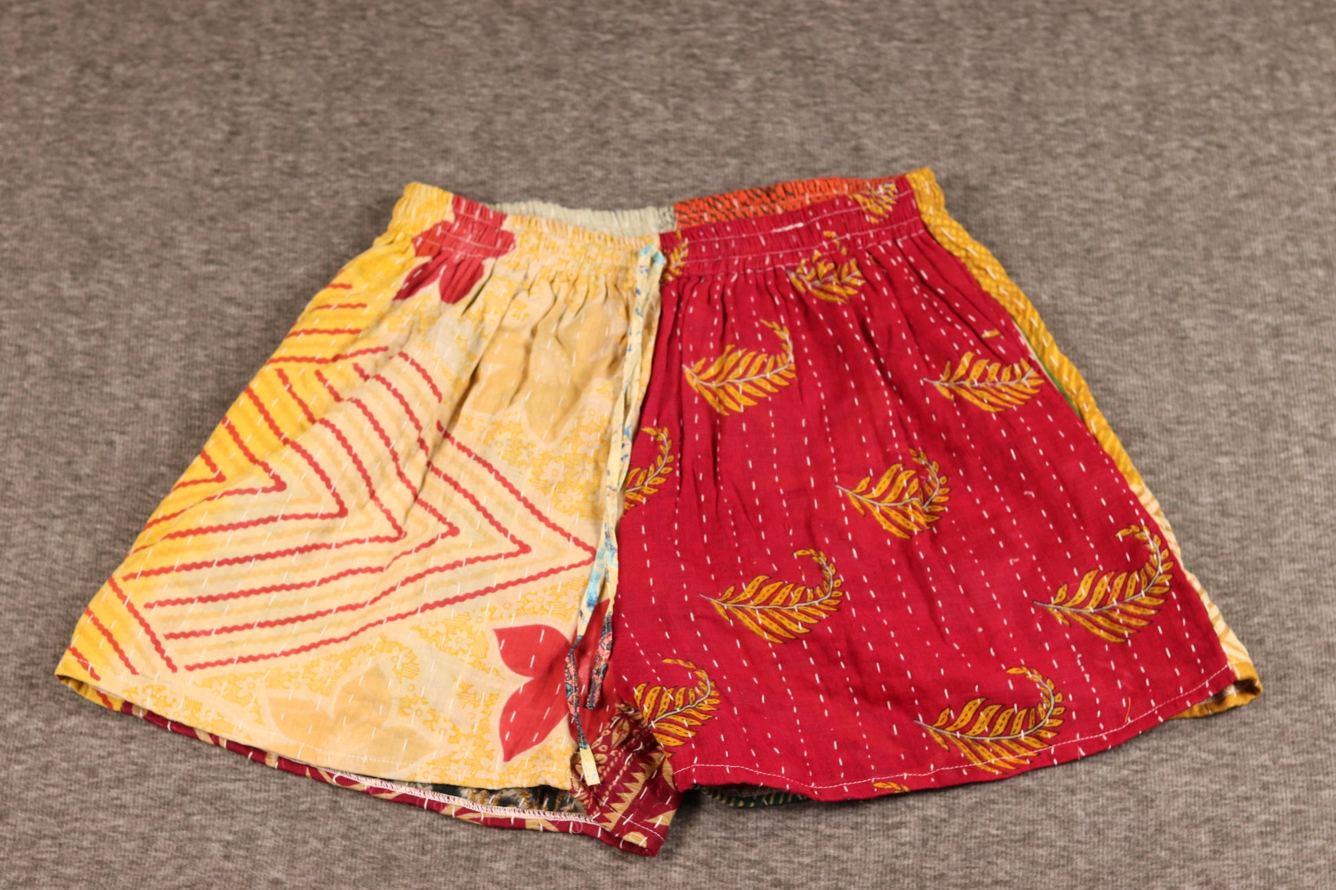Unisex Kantha shorts with golden yellow and crimson cotton panels featuring chevron and leaf prints, detailed with Kantha stitching and a drawstring waist.