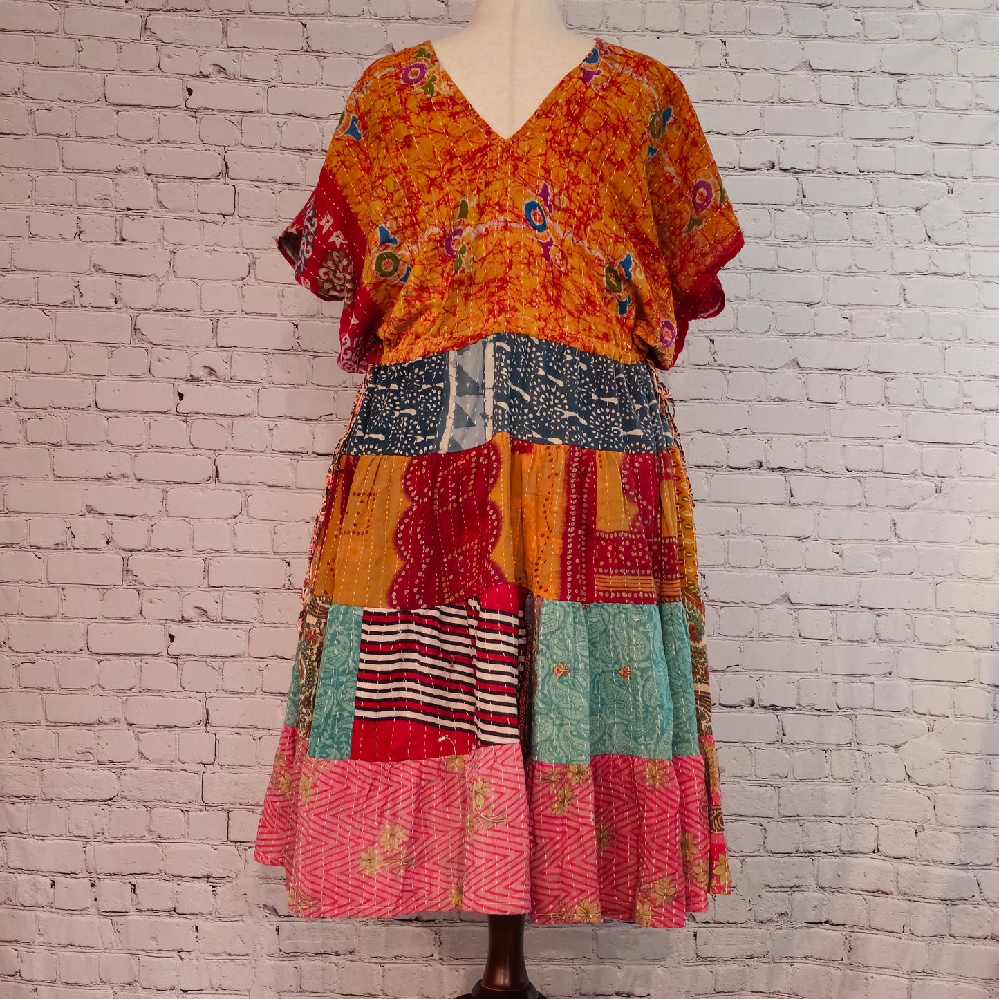 Twillow Saffron Sky Kantha Midi Dress featuring a bright orange floral bodice and colorful patchwork skirt with Kantha stitching detail.