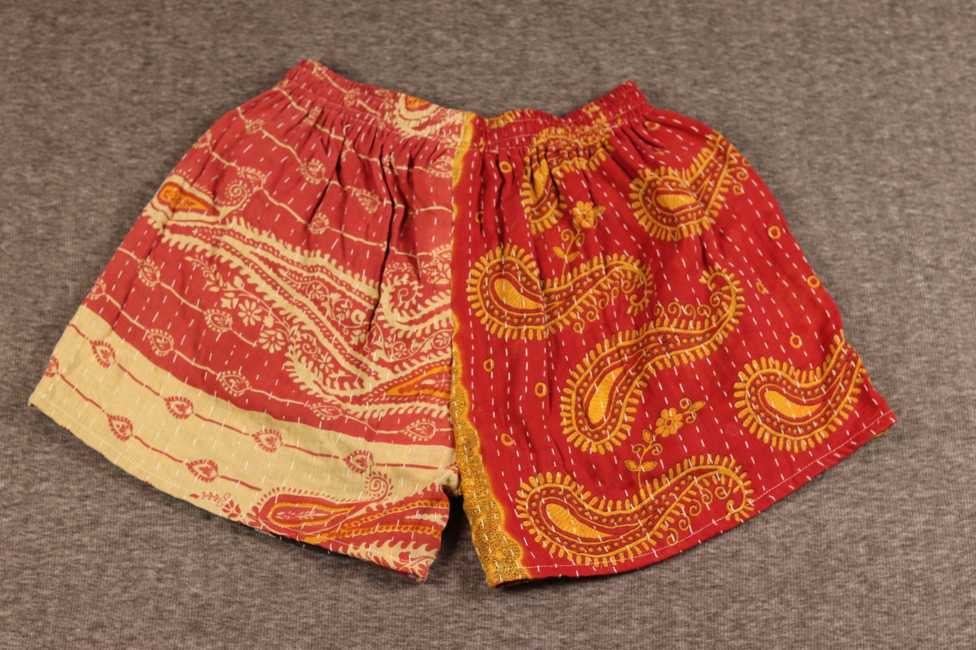 Unisex Kantha patchwork shorts with red and yellow leaf prints and black palm patterns, made from reclaimed cotton sari fabric with handsewn Kantha stitching.