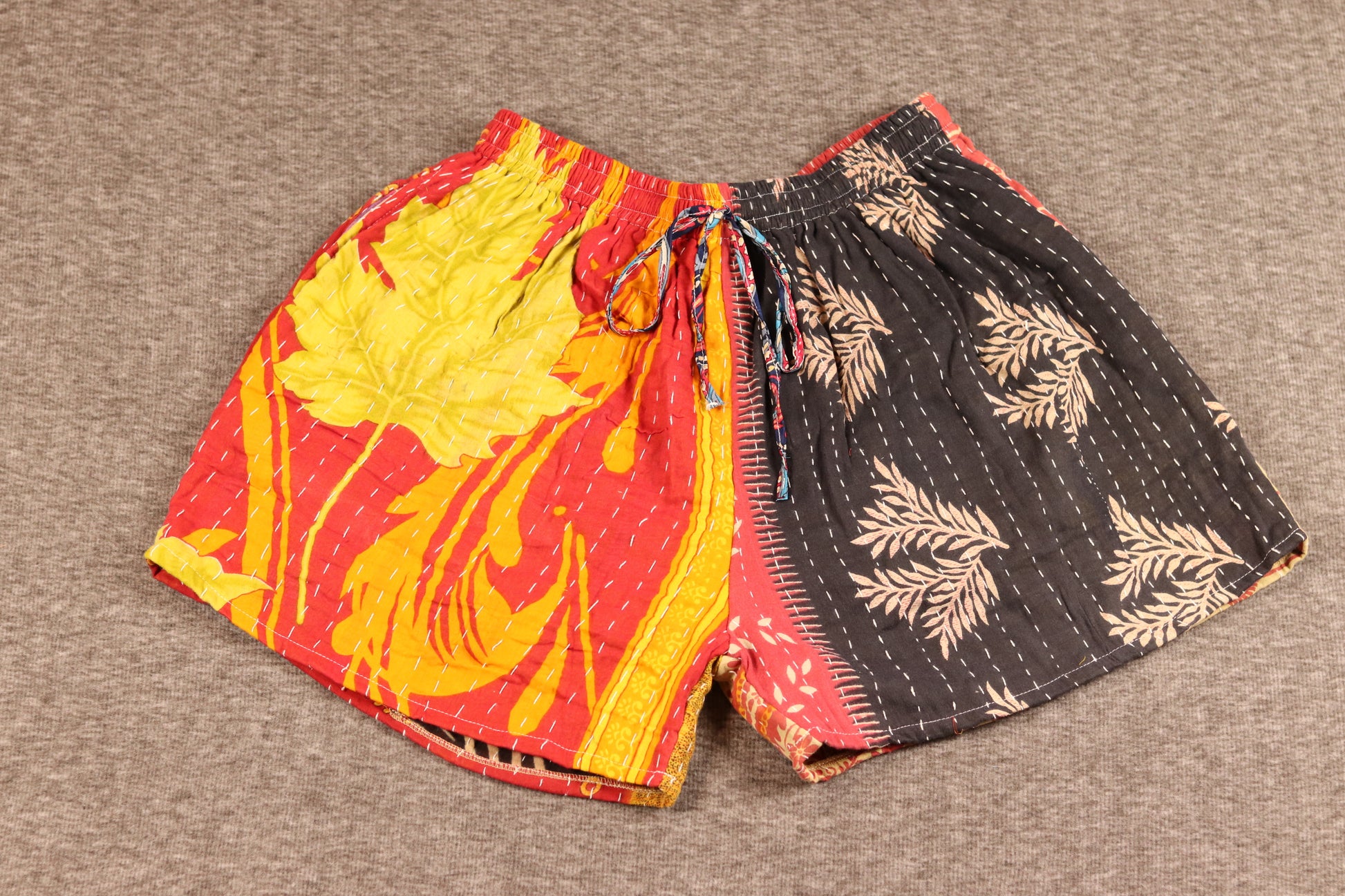 Unisex Kantha patchwork shorts with red and yellow leaf prints and black palm patterns, made from reclaimed cotton sari fabric with handsewn Kantha stitching.