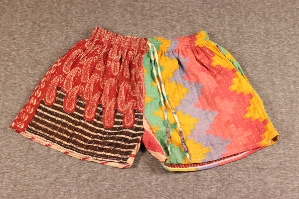 Unisex Kantha shorts with red, orange, green, and cream cotton panels featuring floral and medallion prints, detailed with Kantha stitching and a drawstring waist.