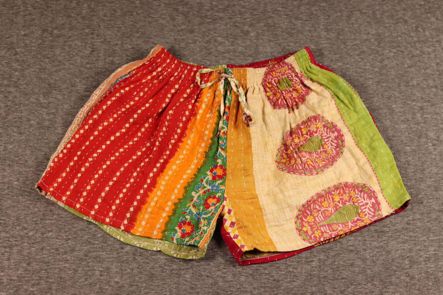 Unisex Kantha shorts with red, orange, green, and cream cotton panels featuring floral and medallion prints, detailed with Kantha stitching and a drawstring waist.