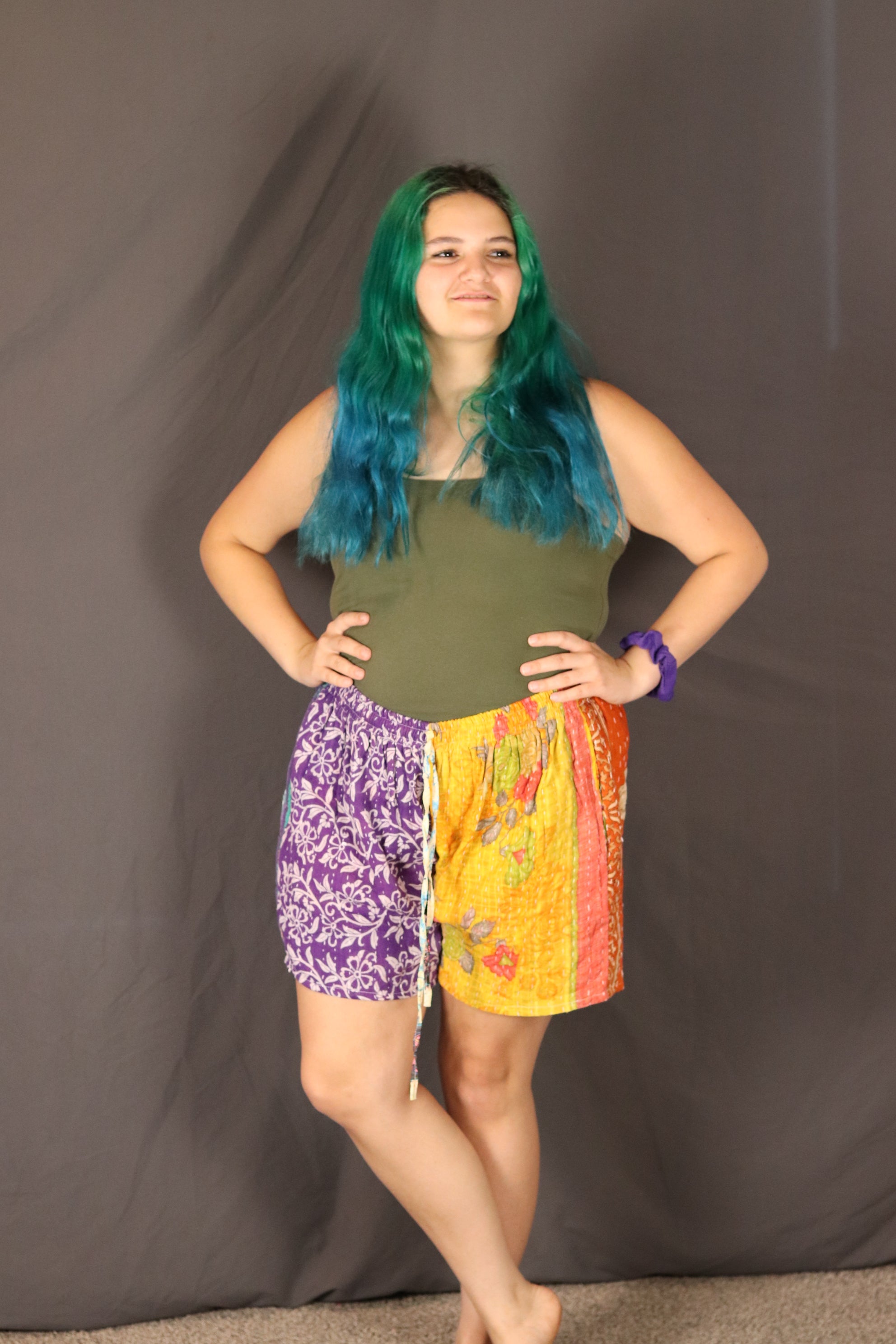 Person with green hair wearing a colorful Kantha shorts.