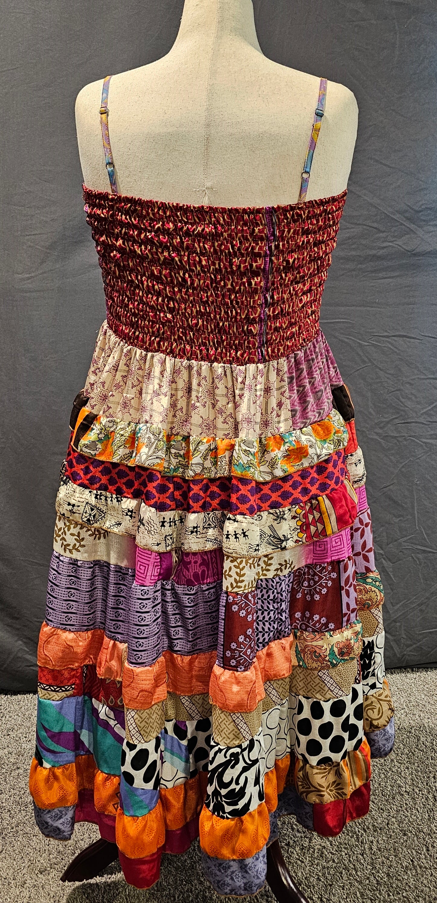 Boho patchwork dress with a red smocked bodice and tiered skirt in orange, purple, and black-and-white patterns, made from recycled sari fabrics by Wild Kantha.