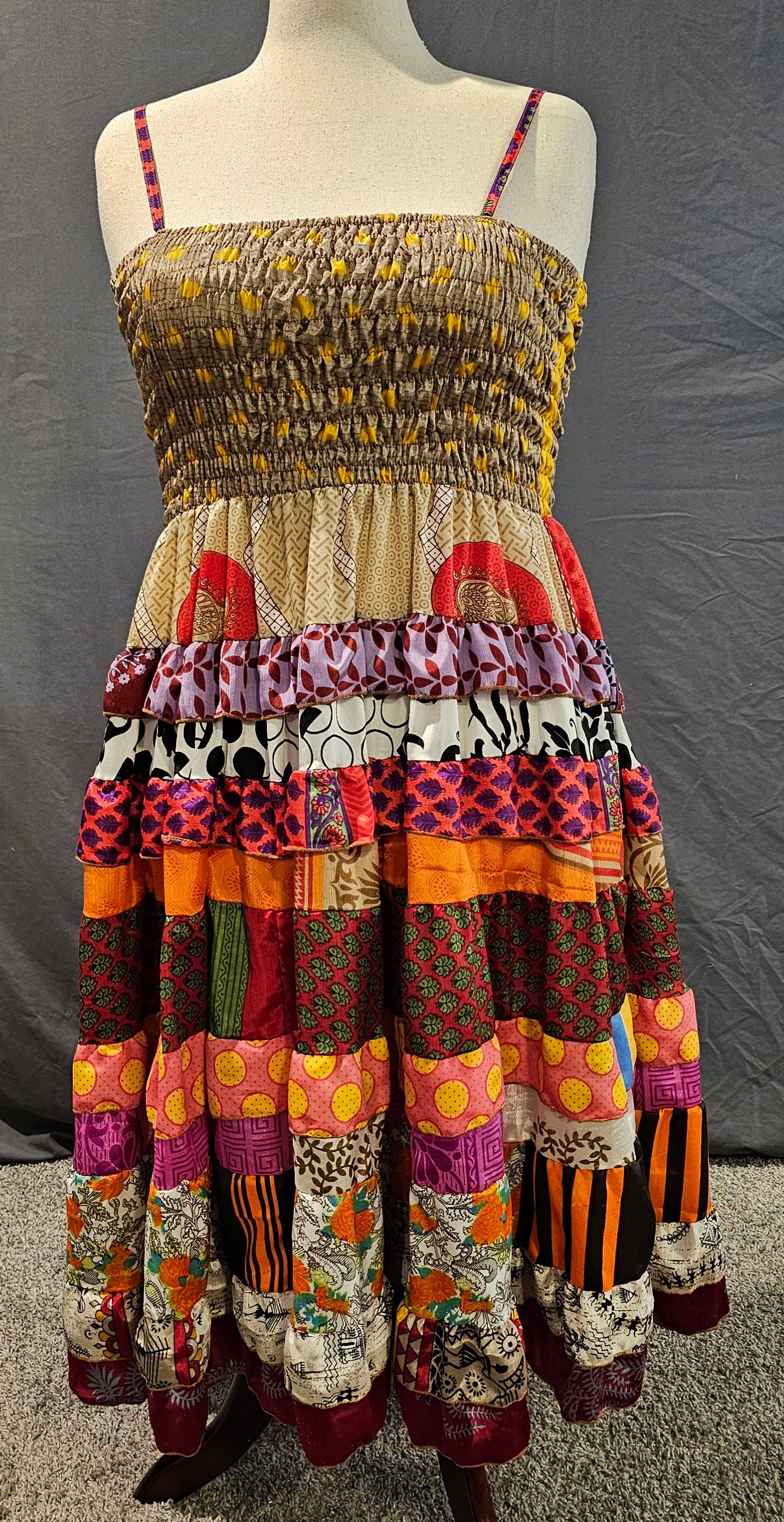 Bohemian patchwork dress with a neutral tan bodice and vibrant red, orange, and yellow tiered skirt, made from recycled sari fabrics.