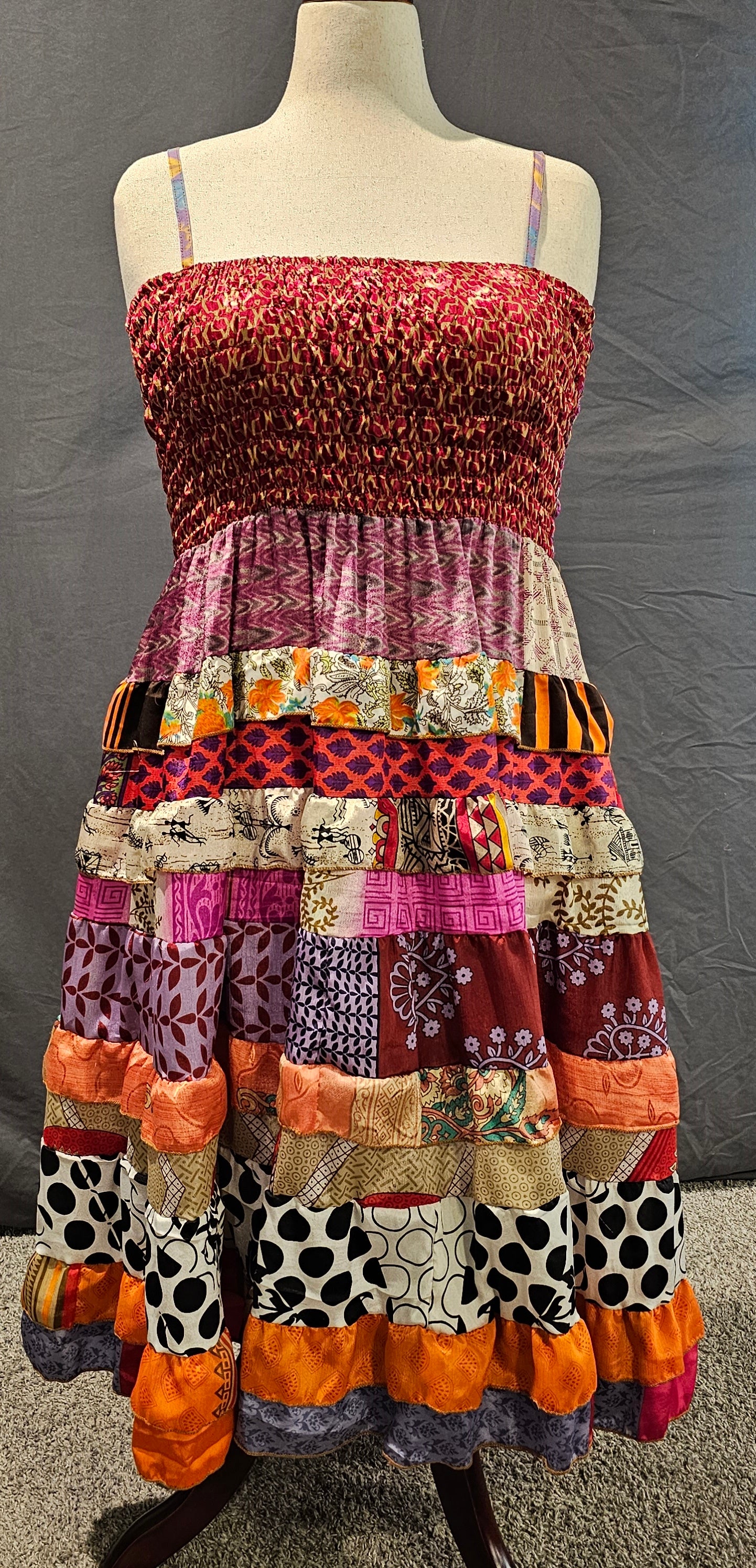 Boho patchwork dress with a red smocked bodice and tiered skirt in orange, purple, and black-and-white patterns, made from recycled sari fabrics by Wild Kantha.