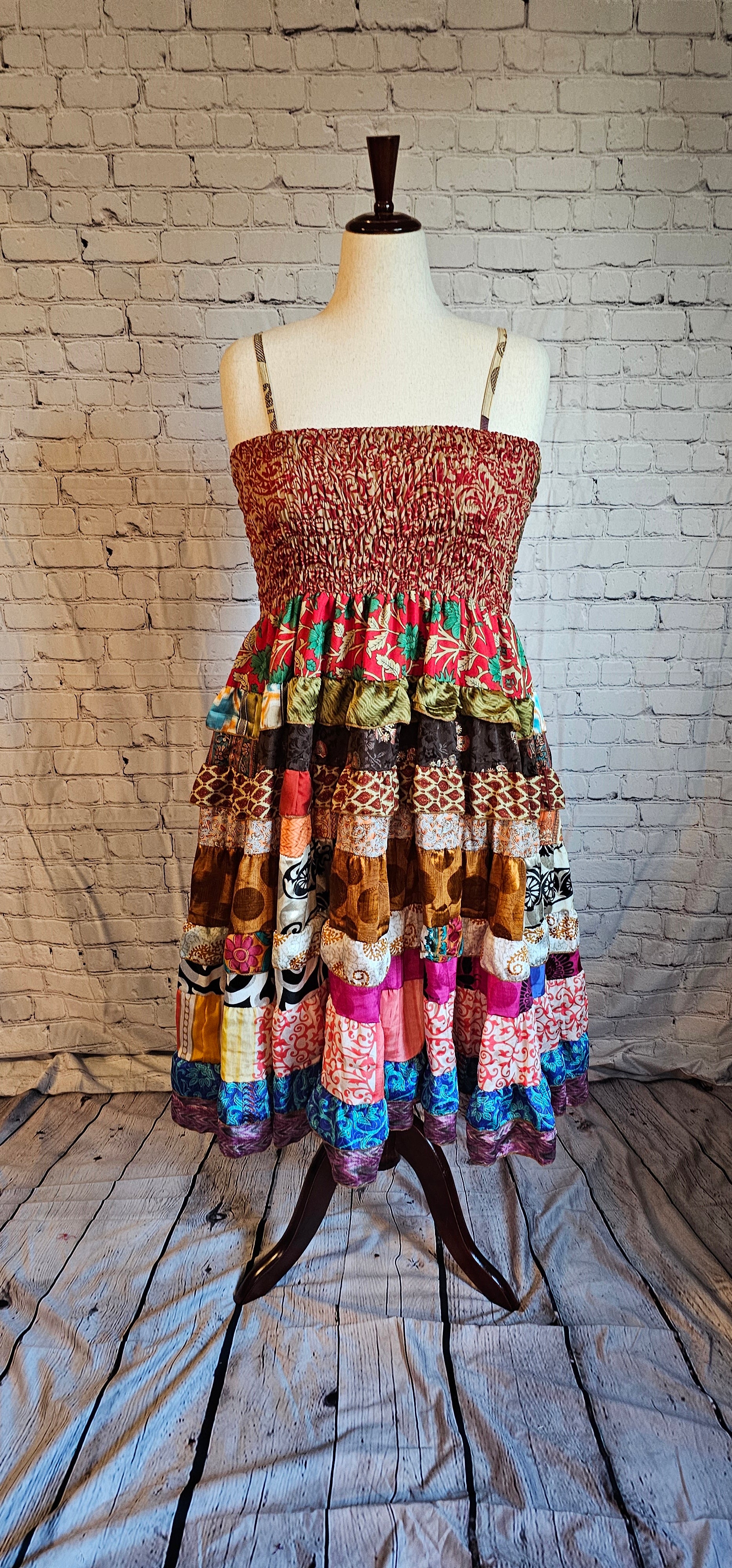 A boho patchwork dress with a ruched red and gold bodice and a tiered skirt of mixed prints in shades of brown, cream, orange, pink, and blue, evoking an earthy autumn palette.