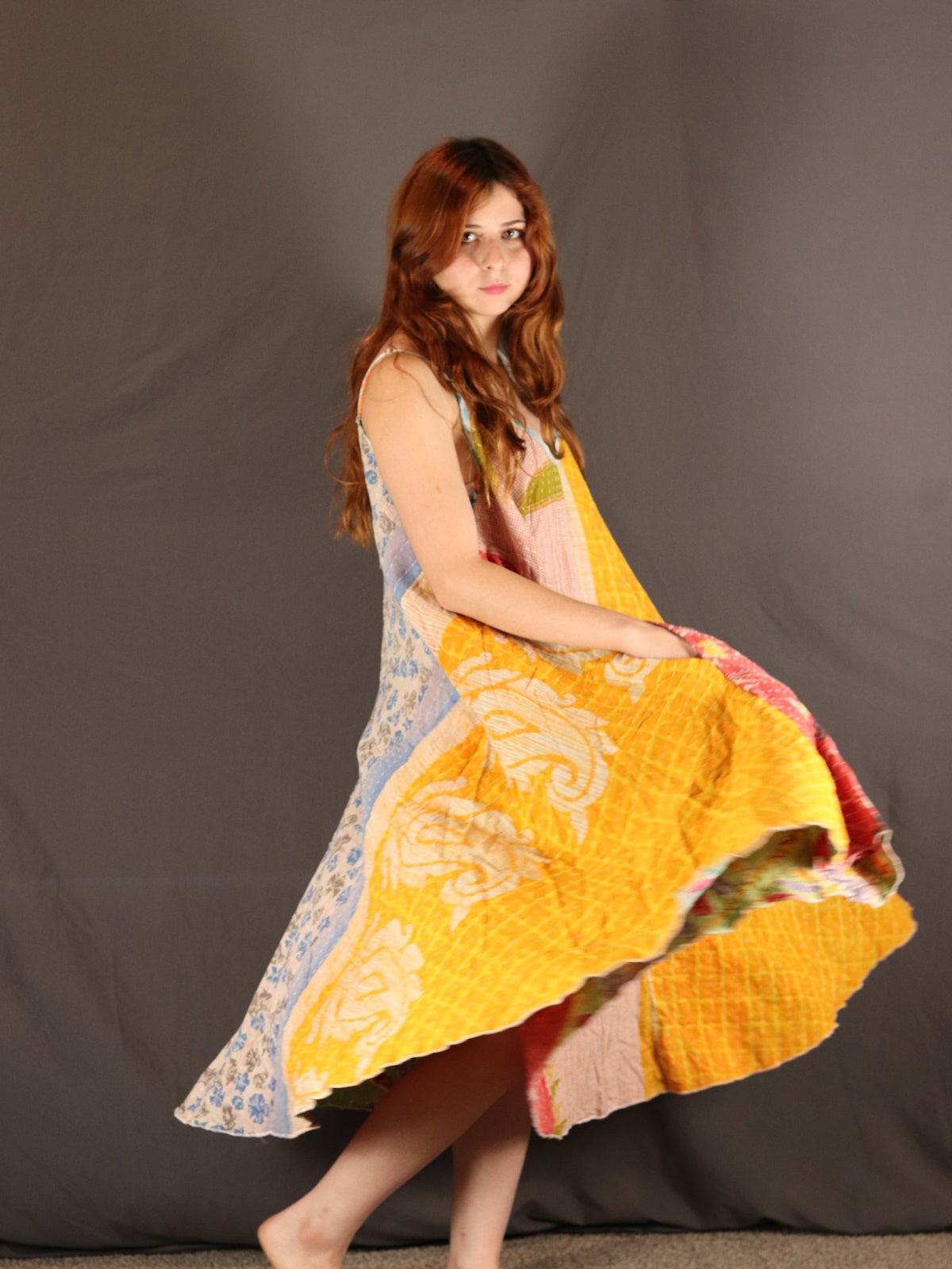 Woman wearing a colorful Kantha dress against a plain background.
