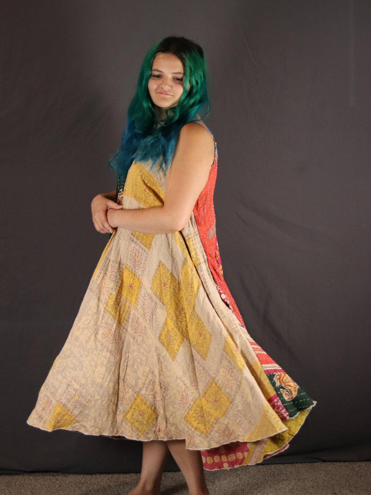 Woman wearing a Kantha colorful dress with a patterned design against a plain background.